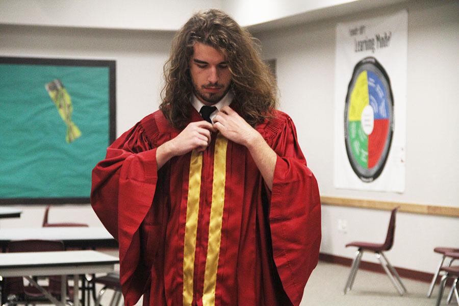 Zane Waggoner puts on a graduation gown for senior pictures