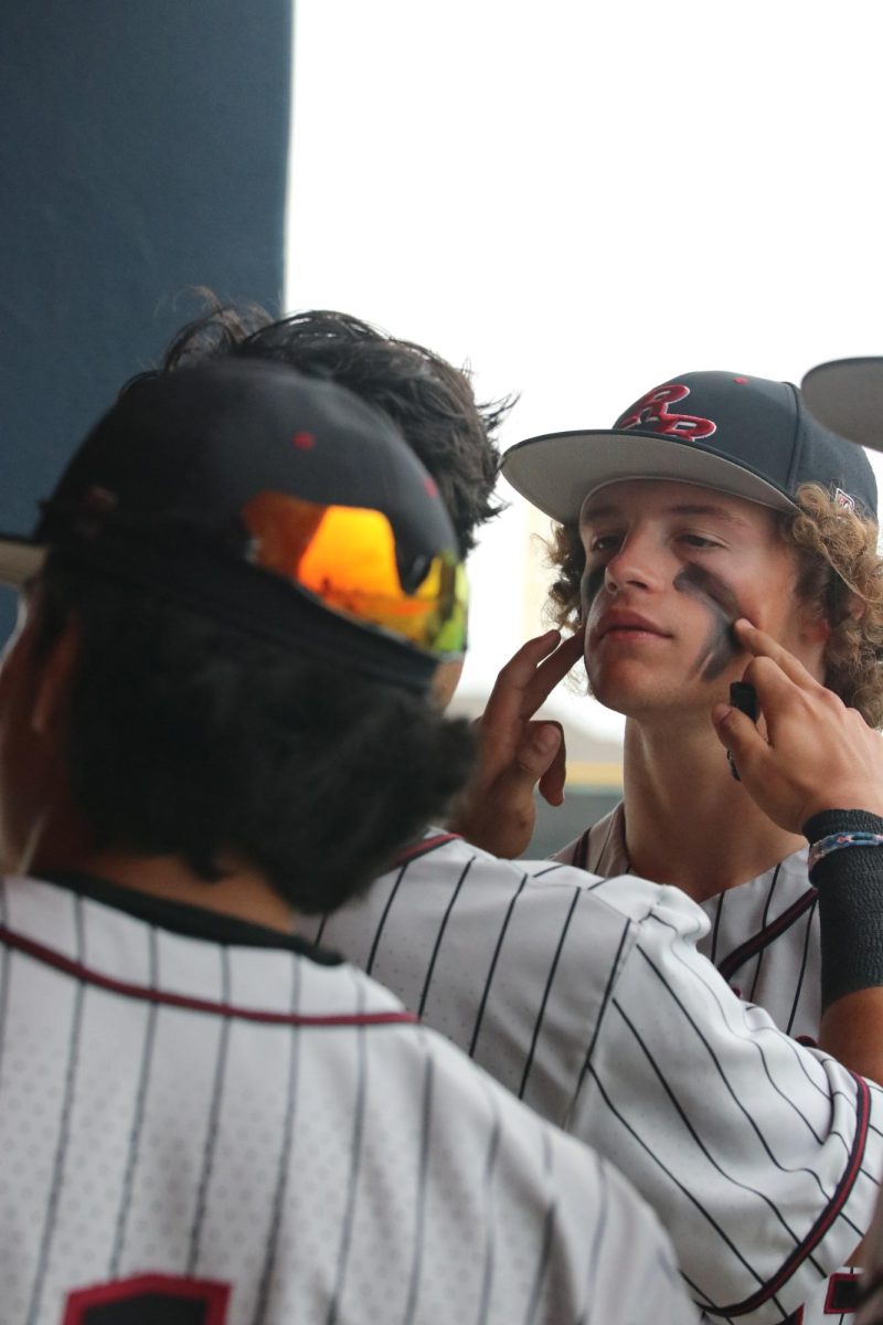 With help from sophomore Jacob Soliz, junior Connor Thompson is painted in eye black. Thompson has played baseball since he was four-years-old and played in the outfield. “I catch fly balls and try to contribute to the team,” Thompson said. “The team is really fun to be around and if you’re successful, you’re having fun.”