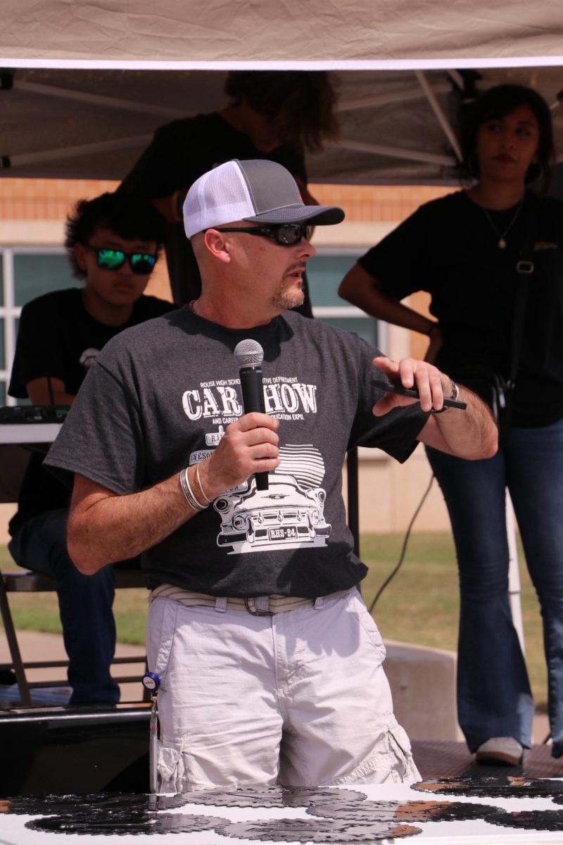 Driven by Passion: At the registration booth, Automotive Tech teacher Jason Glass addresses students and visitors. Glass has played with cars ever since high school, and drew cars and built models. "I love teaching kids things that we all enjoy," Glass said. "If you're taking automotive class, you pretty much enjoy cars, and that's my hobby and love."