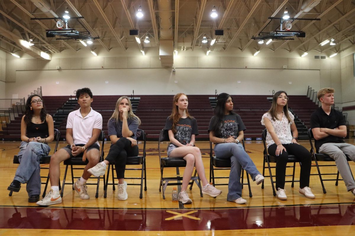 Zoe Clark, David Moon, Natalie Erzal, Connie Cooper, Aradhya Bharti, Jade Corriveau and Connor Privott all sit in the gym in front of the parents and students.  